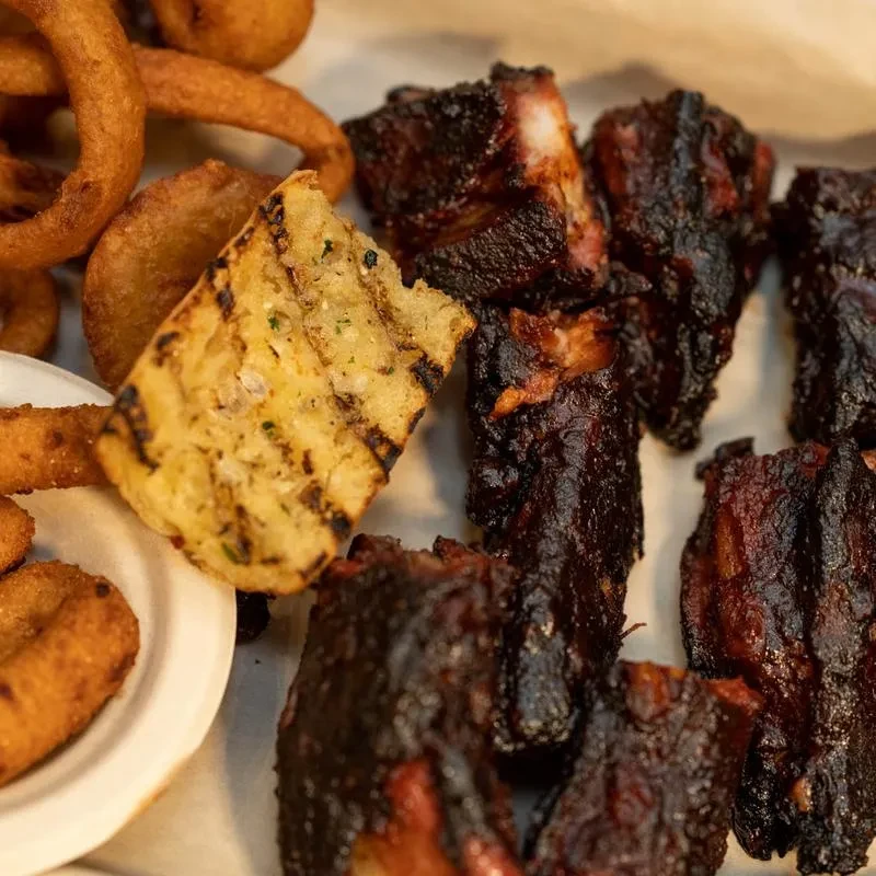 Dark glazed ribs, crispy onion rings, and grilled bread on a platter.