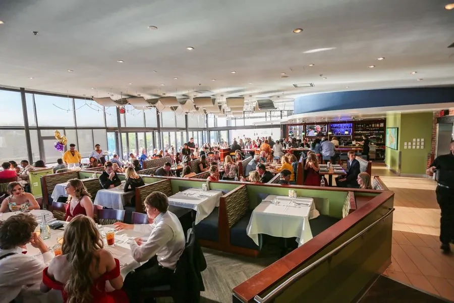 Busy restaurant dining room with patrons, booths, tables, and bar.