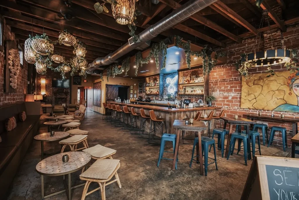 Rustic eclectic bar with brick walls, wooden bar, and unique lighting.