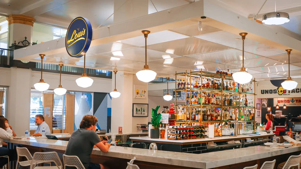 Restaurant interior with patrons at a marble bar and 'Louis' sign.