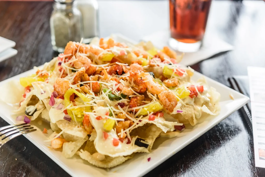 Close-up of loaded shrimp nachos with sauce, cheese, and vegetables.