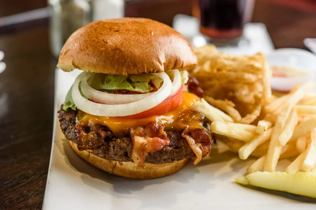 Bacon cheeseburger, french fries, and dill pickle spear on a white plate.