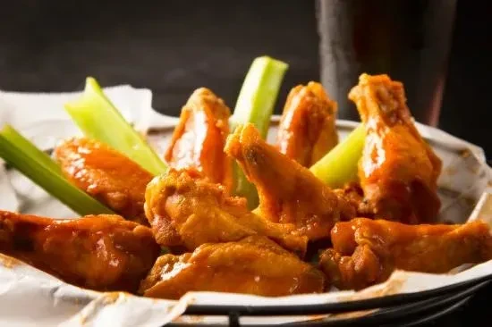 Glossy buffalo chicken wings and celery sticks in a basket.