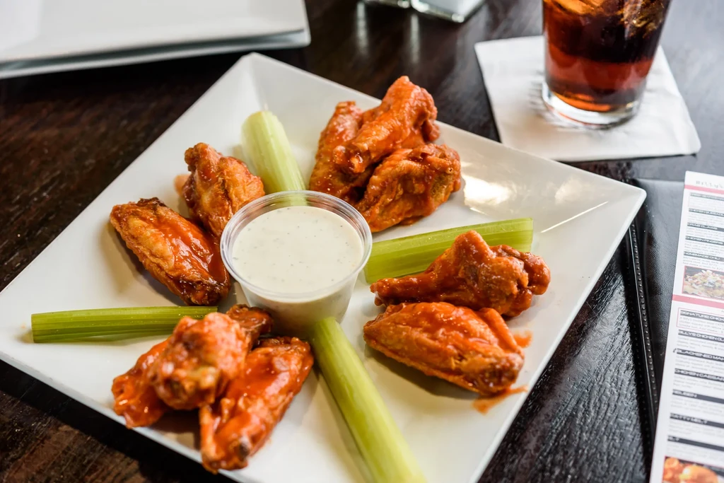 Overhead view: buffalo chicken wings, celery sticks, and dip on a plate.