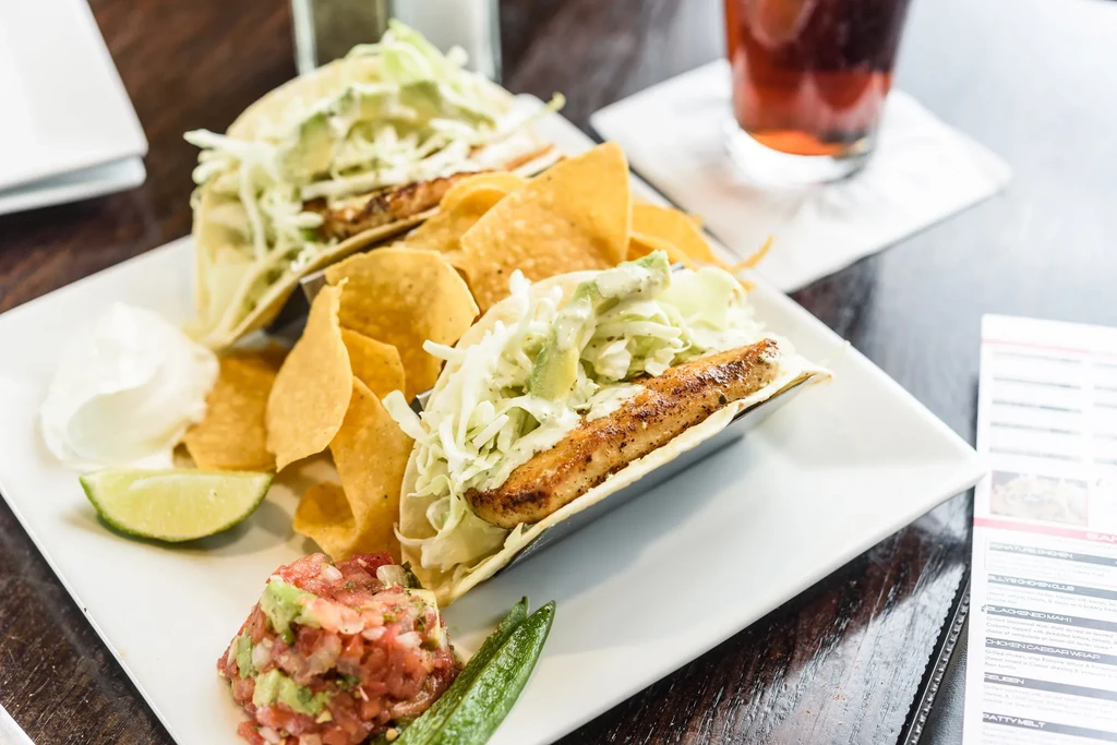 Two fish or chicken tacos with chips, salsa, and lime on a plate.