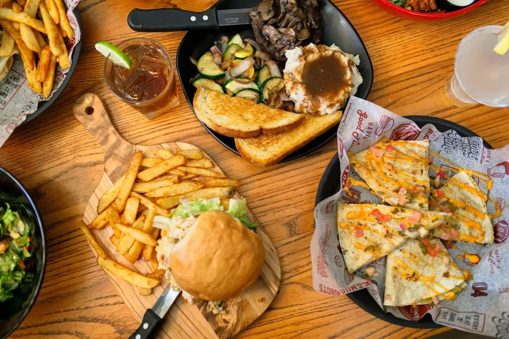 Wooden table laden with steak, sandwich, quesadilla, fries, and two drinks.