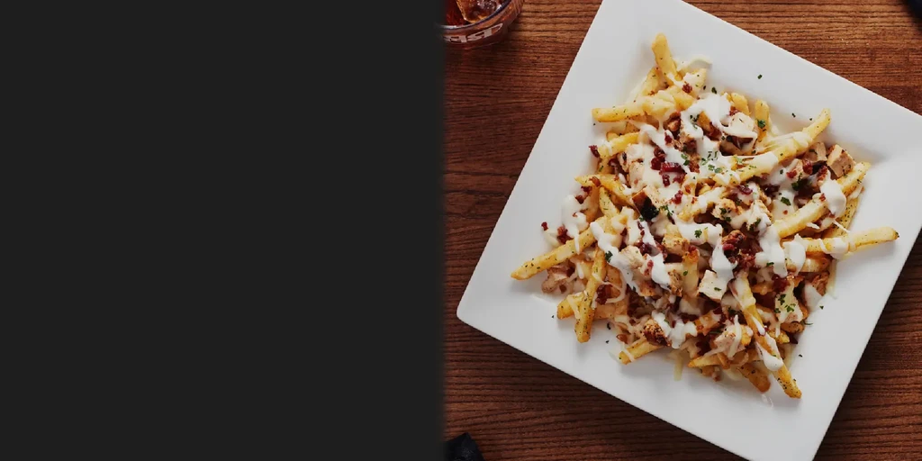 Loaded french fries with creamy sauce, bacon, chicken, and green herbs.