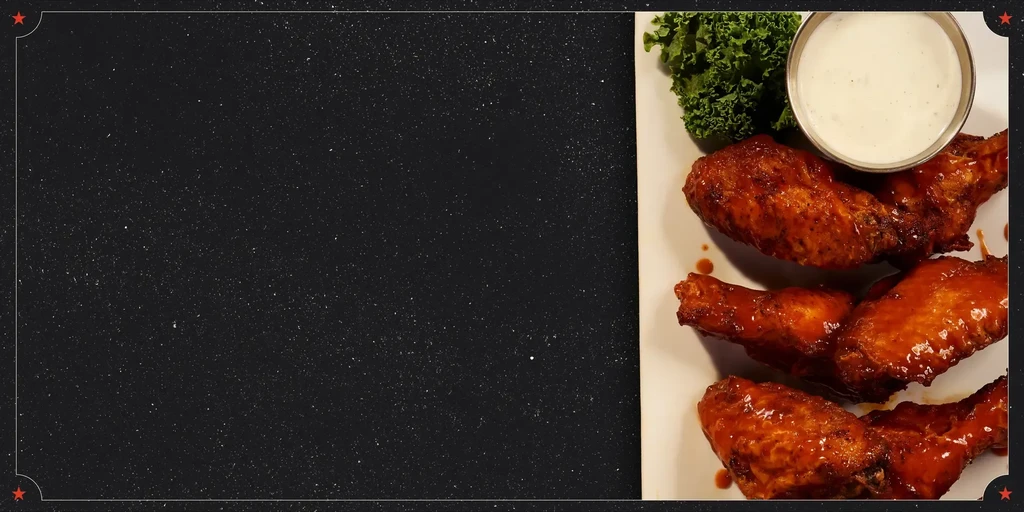 Reddish-orange chicken wings, creamy dip, and greens on a white plate.