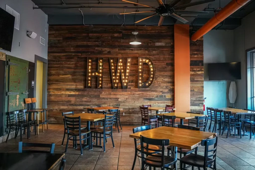 Empty rustic-industrial restaurant with 'HWD' marquee on wood wall.