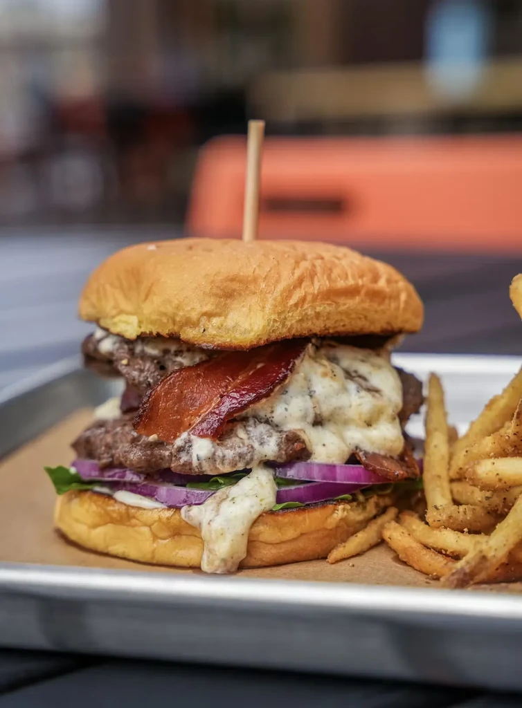 Stacked beef burger with bacon, creamy sauce, lettuce, and fries.