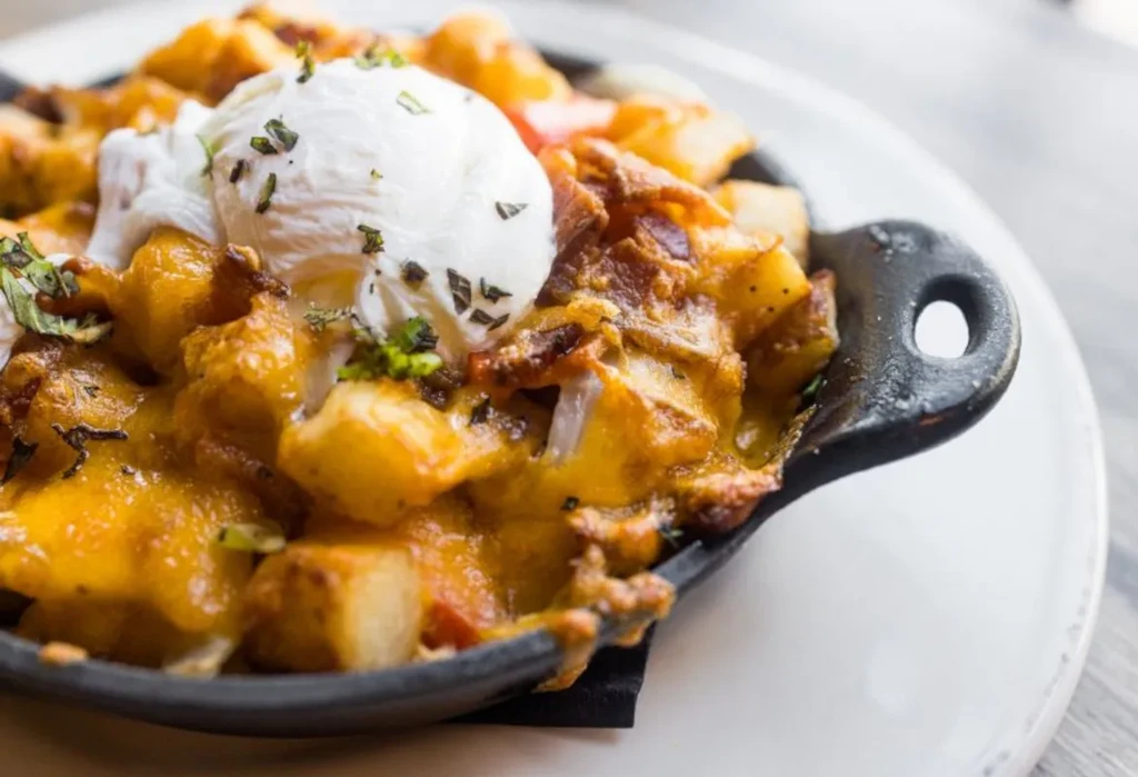 Poached egg over cheesy potatoes and bacon in a cast iron skillet.