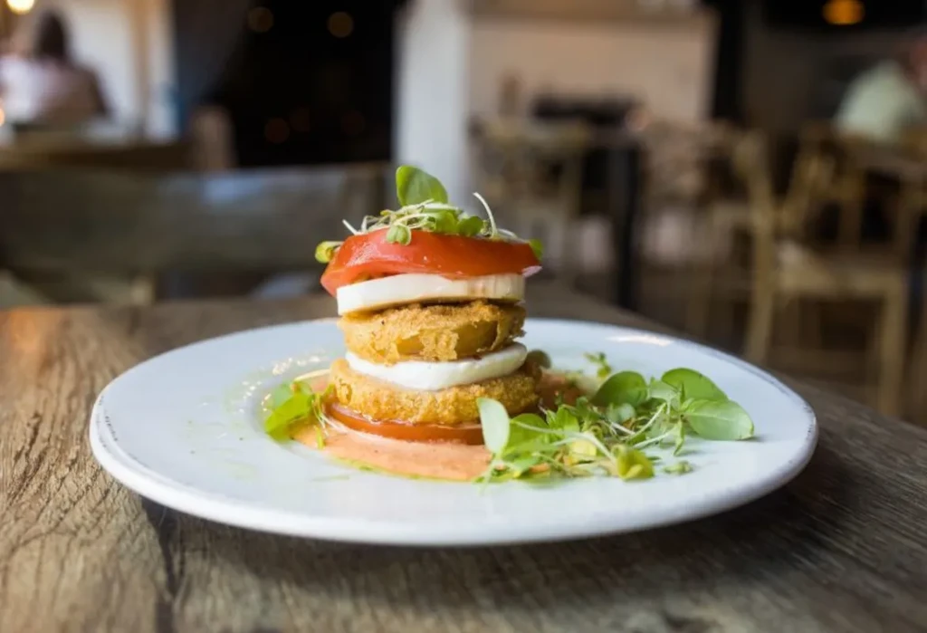 Stacked golden-brown fried items, mozzarella, tomato, garnished with greens.