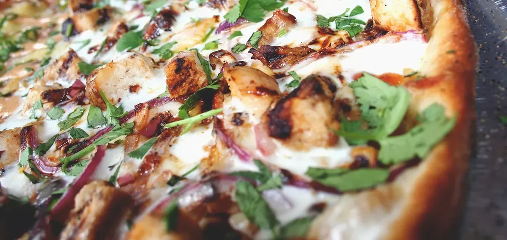 Pizza with white sauce, grilled chicken, red onion, and green herbs.