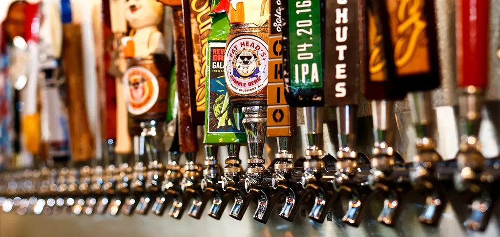 Detailed beer tap handles with various designs and branding at a bar.