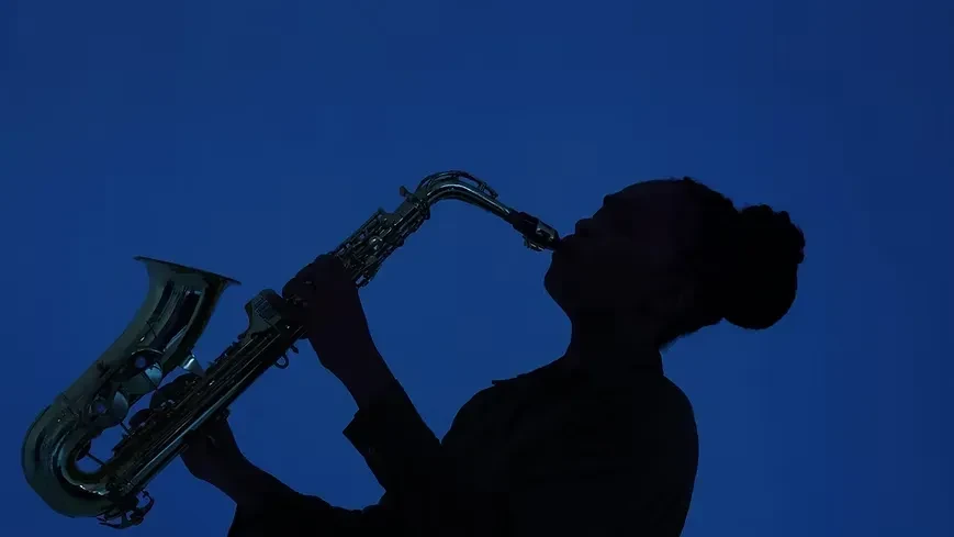 Silhouetted musician playing saxophone, metallic gleam, deep blue background.