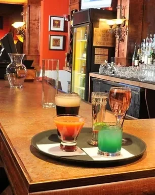 Five colorful drinks on a tray at a warmly lit bar.