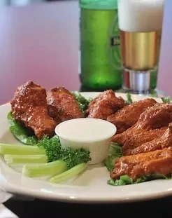Plate of crispy buffalo wings with celery, dipping sauce, and beer.