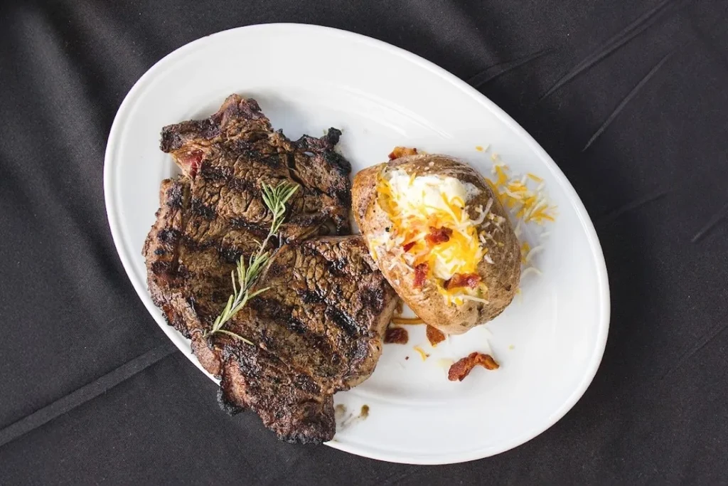 Grilled steak with rosemary and loaded baked potato on a plate.