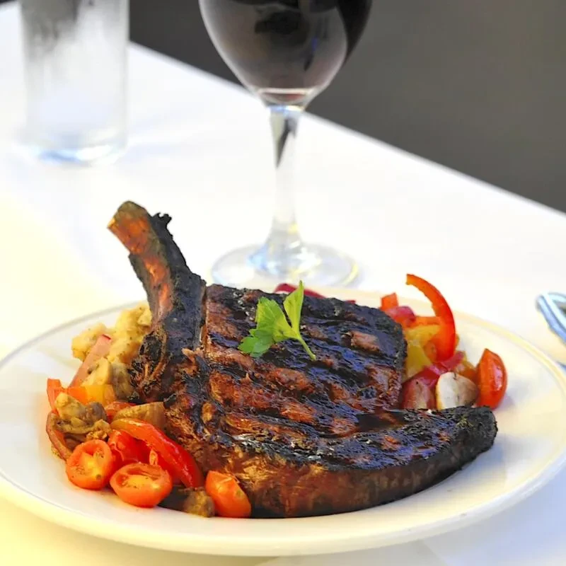 Close-up of grilled bone-in steak with herb, vegetables, and mashed potatoes.