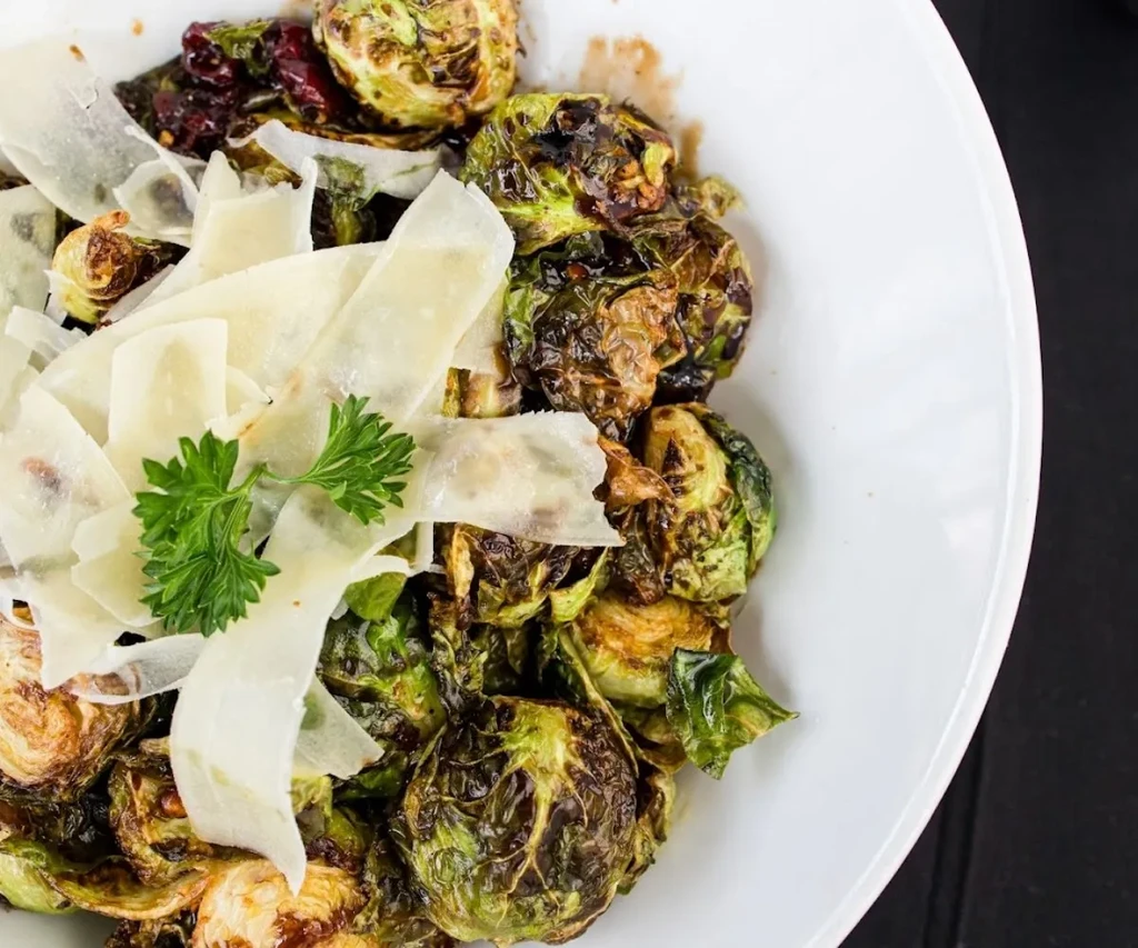 Roasted Brussels sprouts with cheese shavings and parsley in a white bowl.