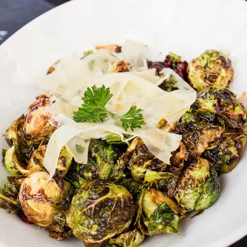 Charred roasted Brussels sprouts in a bowl with cheese and parsley.