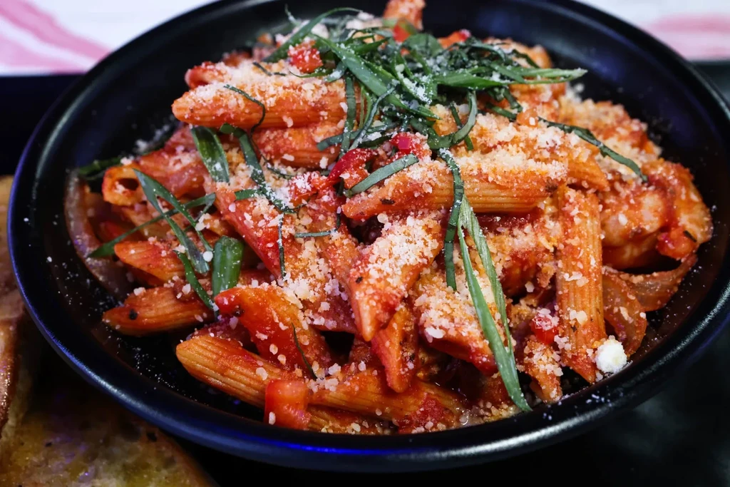 Penne pasta with tomato sauce, cheese, and herbs in a dark bowl.