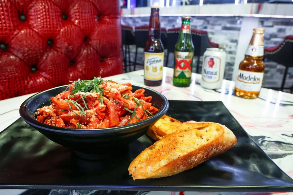 Penne pasta in red sauce with bread and beers at a restaurant.