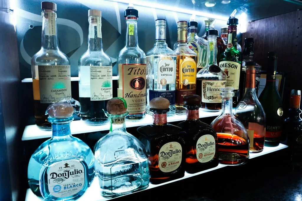High-end liquor bottles on tiered, illuminated bar shelves.