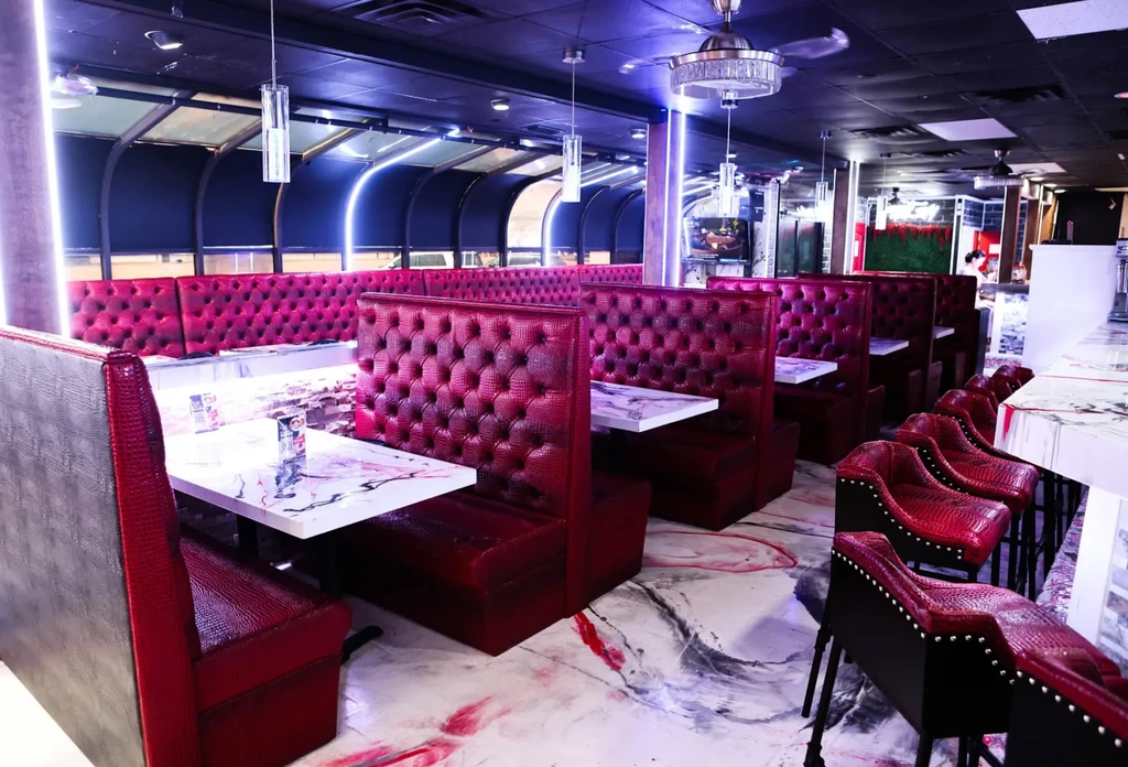 Empty, modern restaurant interior featuring red booths, marble tables, and patterned floor.