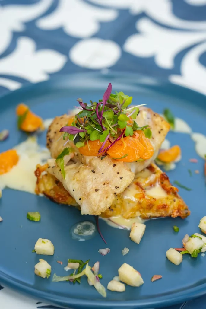 Pan-seared fish on crispy base with orange, microgreens, and sauce.