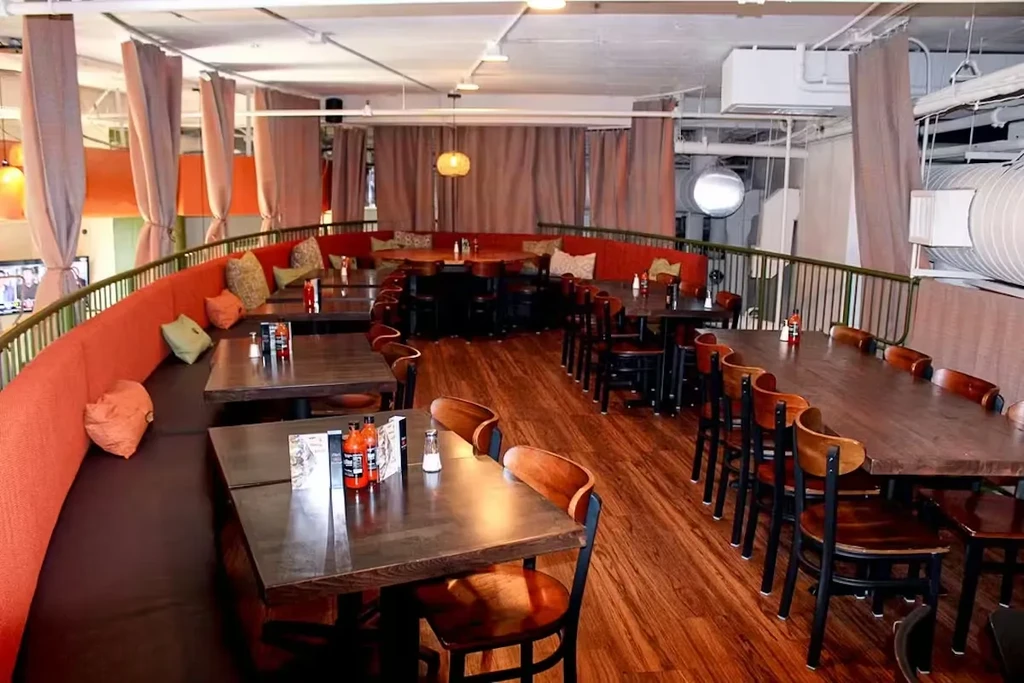 Empty modern industrial-chic restaurant with orange banquette and tables.