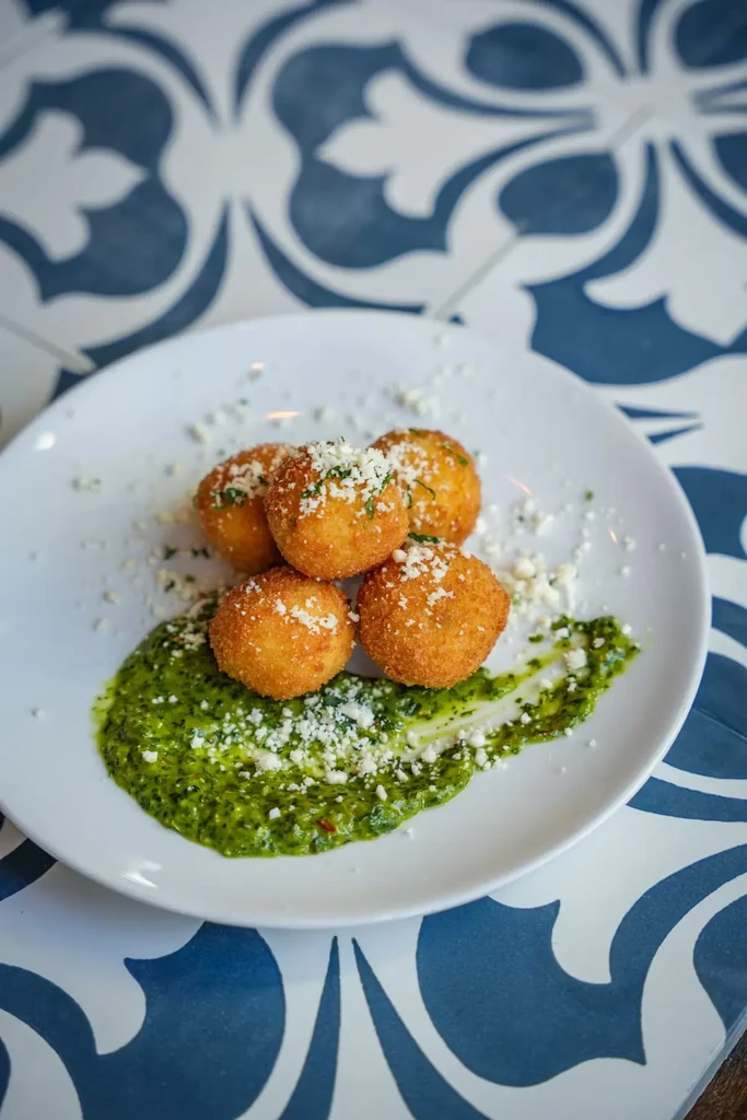Golden fried spheres with cheese, herbs, and green sauce on a plate.
