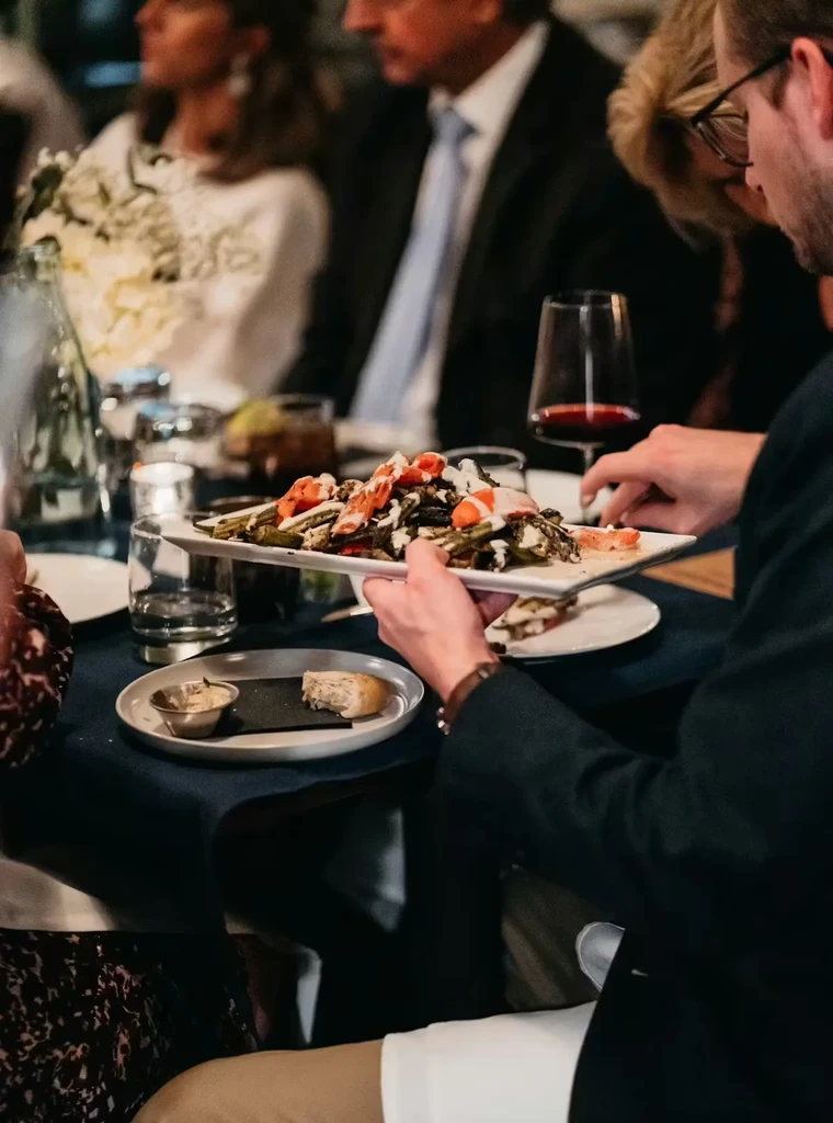 Hands serving artfully plated vegetables with white sauce at dinner.