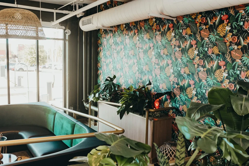 Restaurant interior with dark green tropical wallpaper and velvet booth.
