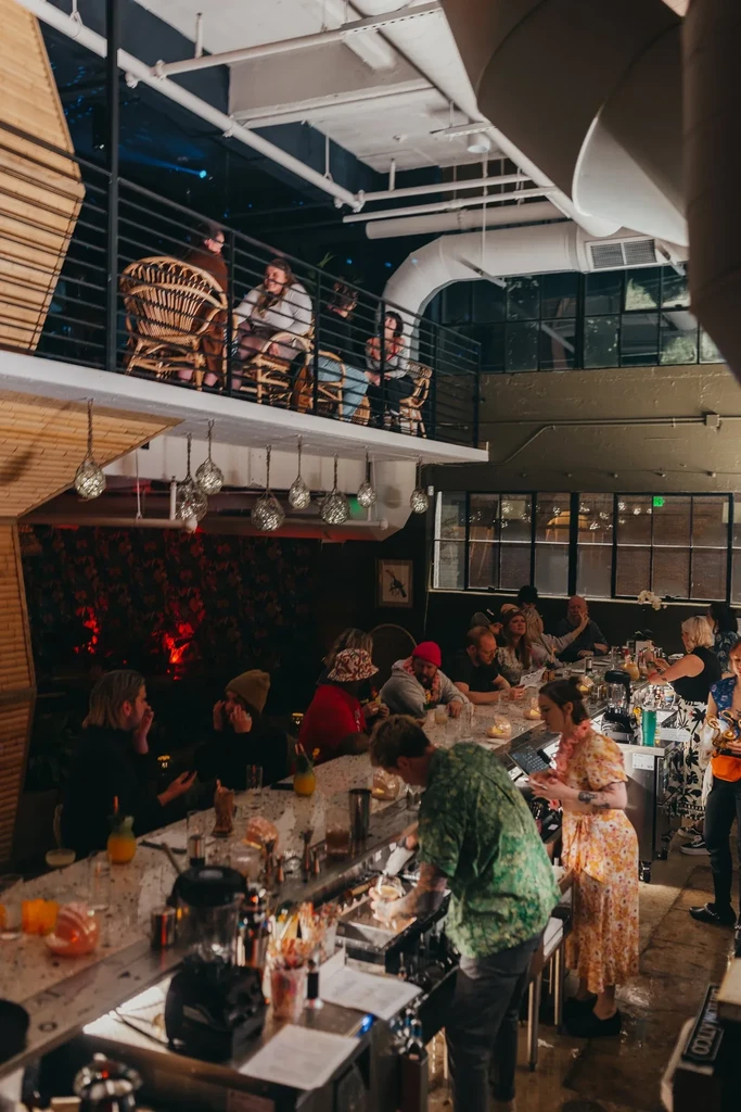 Two-story bar interior bustling with patrons, bartenders, and distinct industrial design.