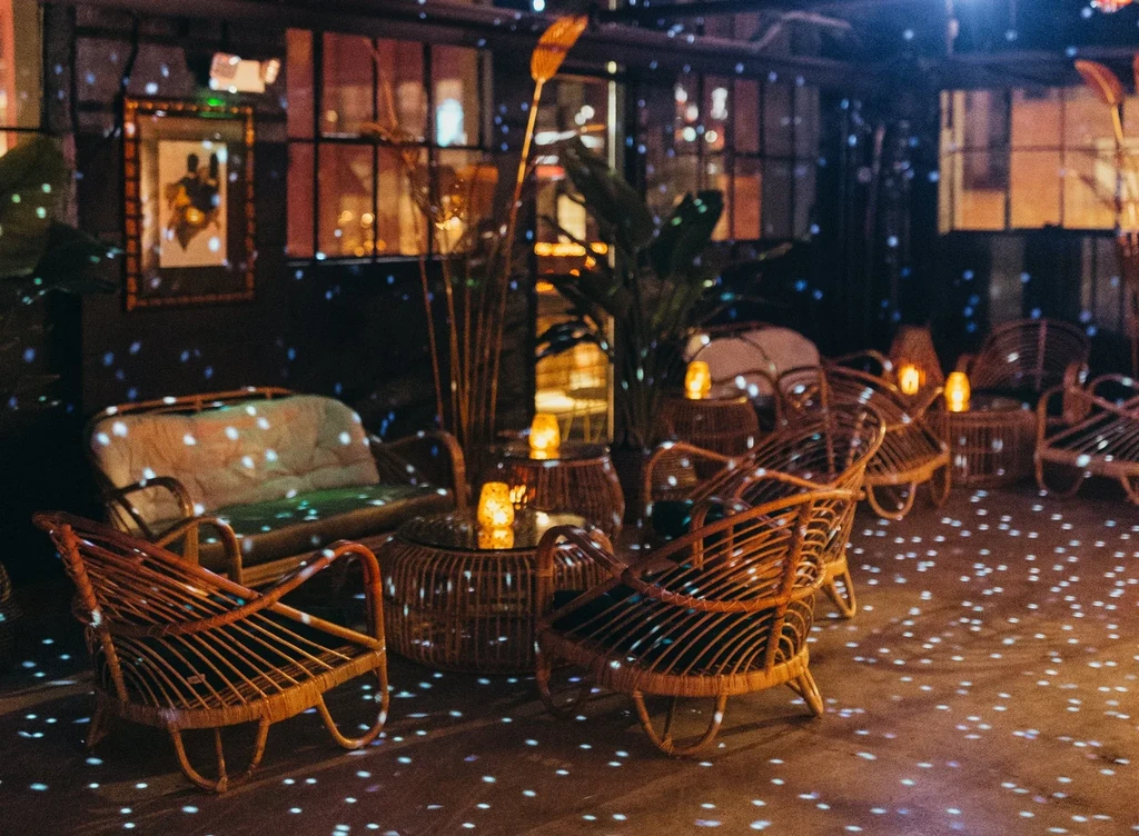Atmospheric lounge with rattan furniture and patterned floor lighting.