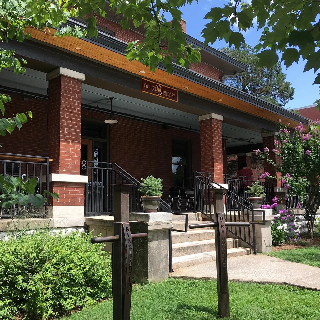 Red-brick Frothy Monkey cafe, covered porch, green foliage, bike parking.