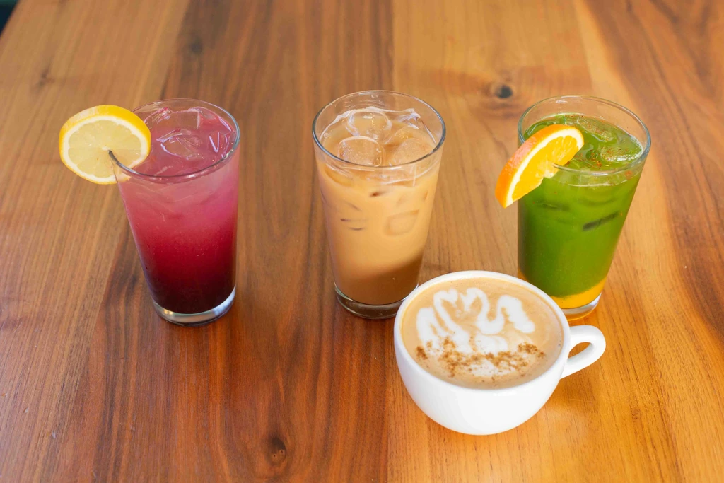 Four assorted iced drinks and a latte on a wooden table.