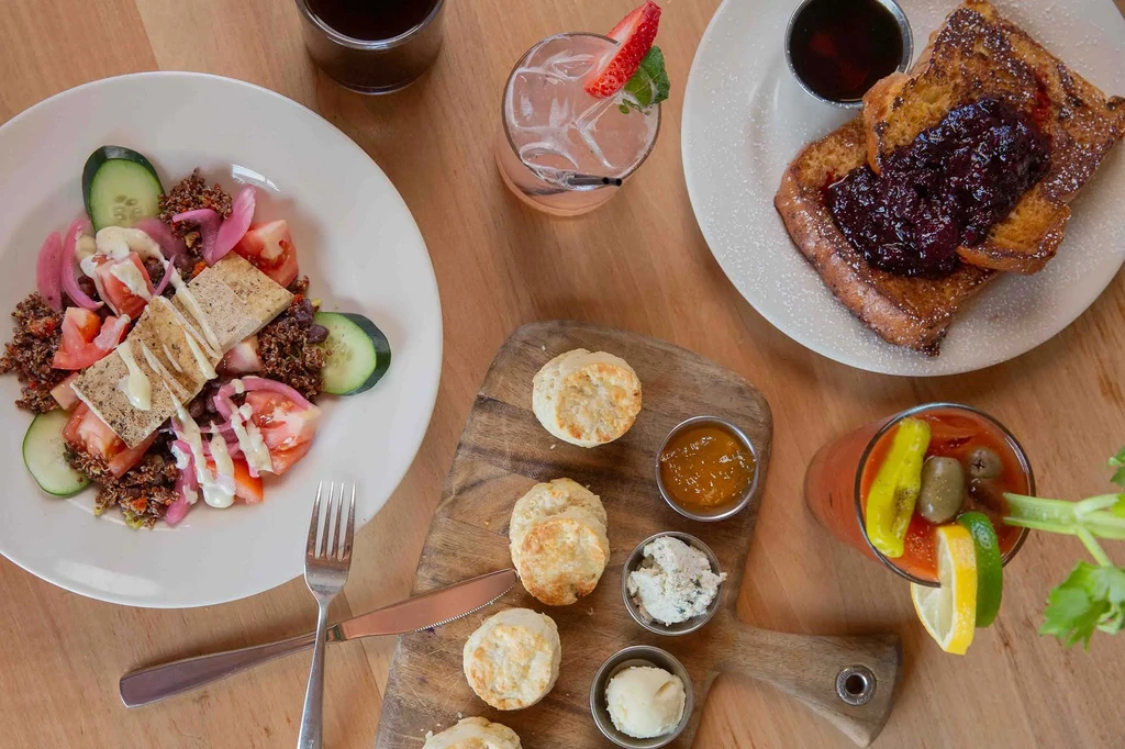 Overhead spread of French toast, quinoa salad, biscuits, and various drinks.