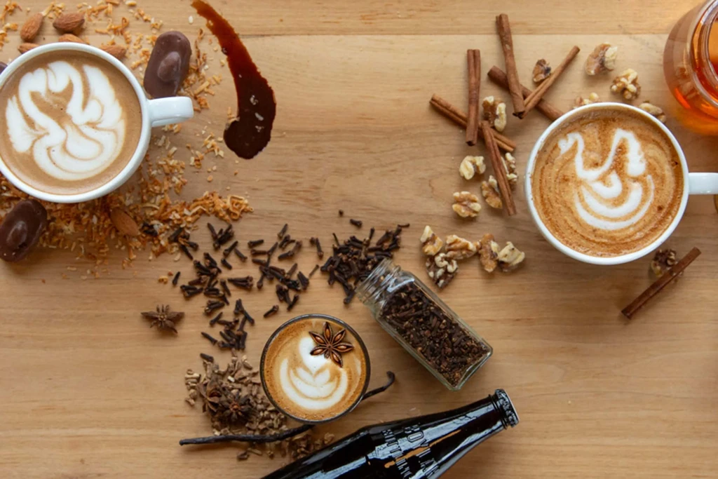 High-angle flat lay of three coffees with latte art, spices, nuts.