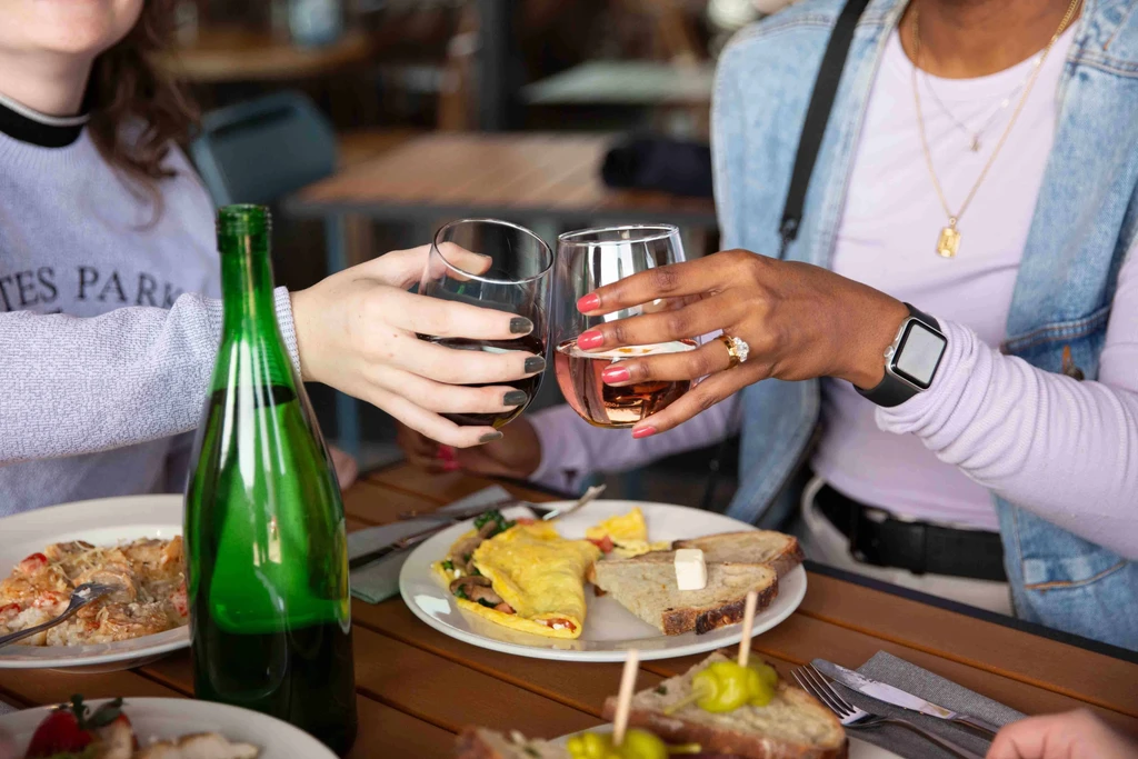Hands toasting red and rosé wine glasses on a table of food.