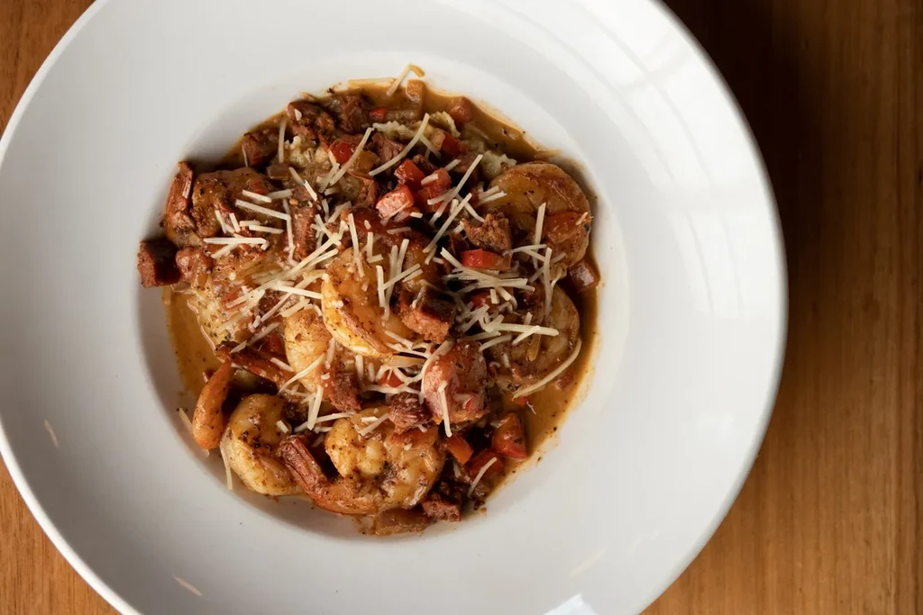 Creamy shrimp and sausage with cheese in a white bowl.