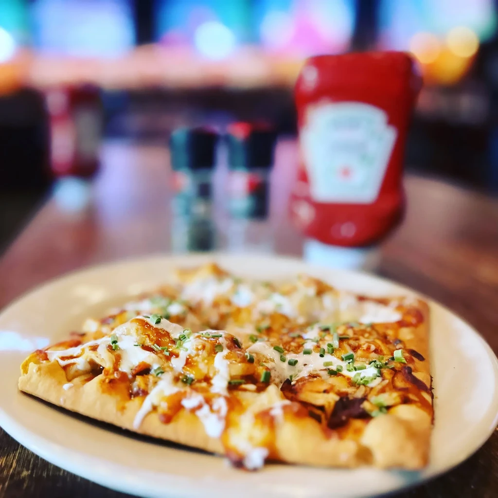 Chicken barbecue flatbread with creamy sauce and chives on a white plate.