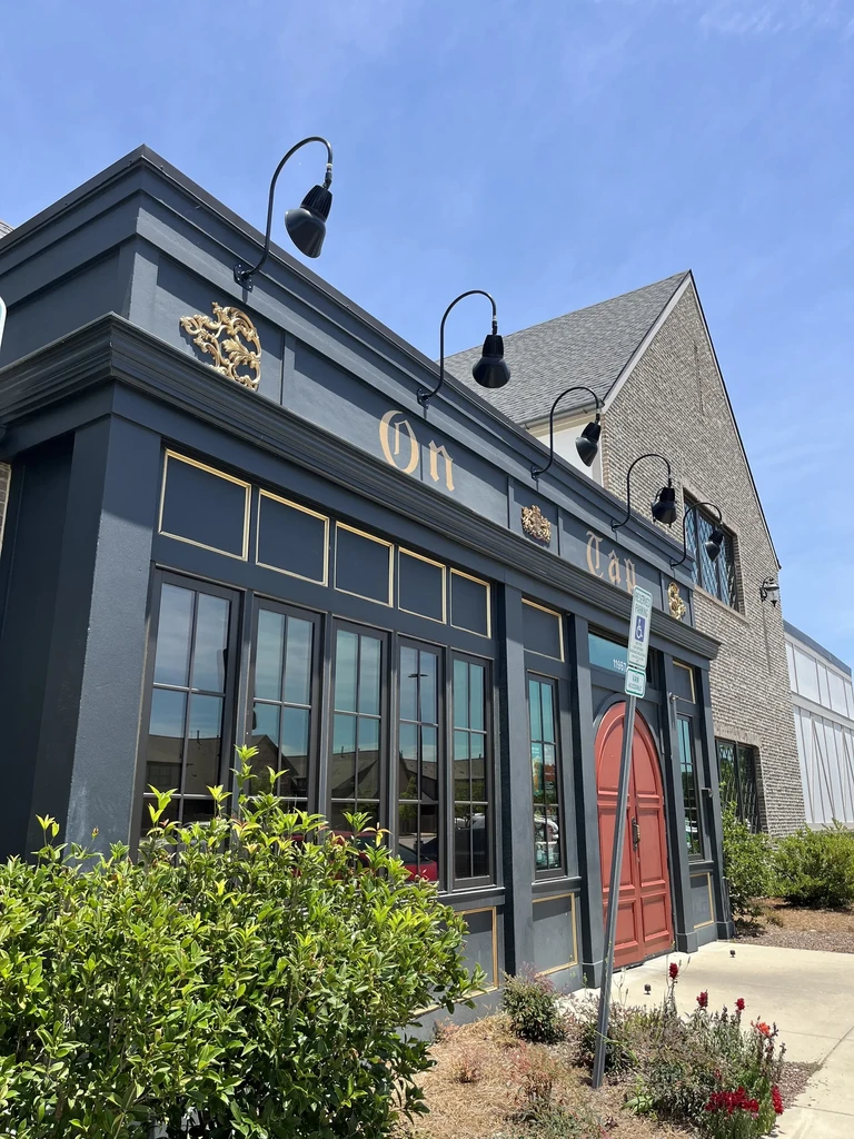 Dark grey-blue restaurant facade with gold details and a red arched door.