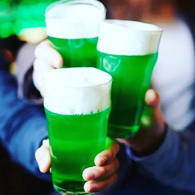 Hands toast three pint glasses of green beer with white foam.