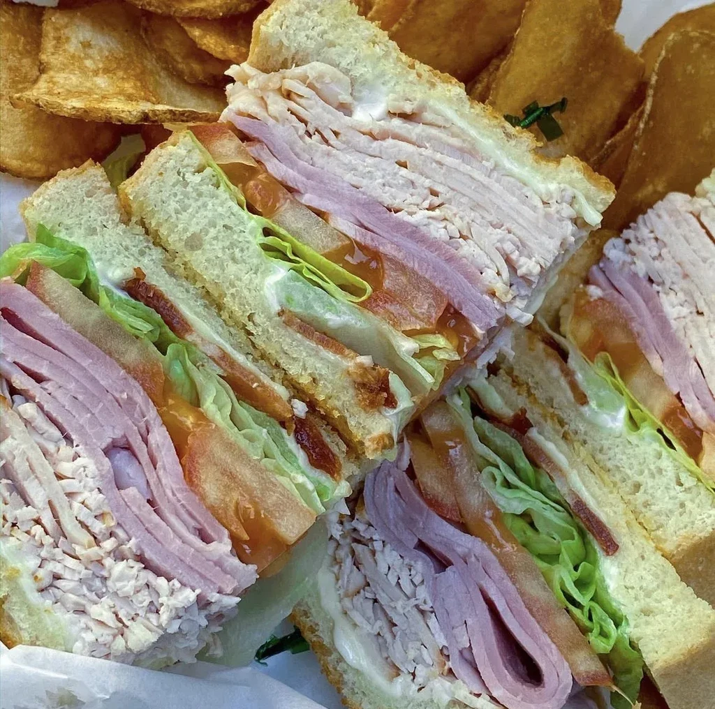 Quartered club sandwich with ham, turkey, lettuce, tomato, and potato chips.