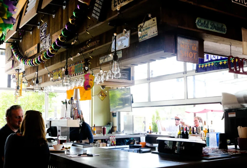 Mardi Gras themed bar interior with beads, rustic signs, and patrons.