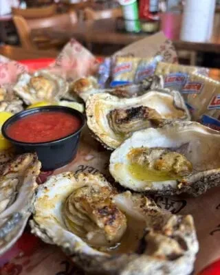 Grilled and raw oysters on a platter with sauce, lemon, and crackers.