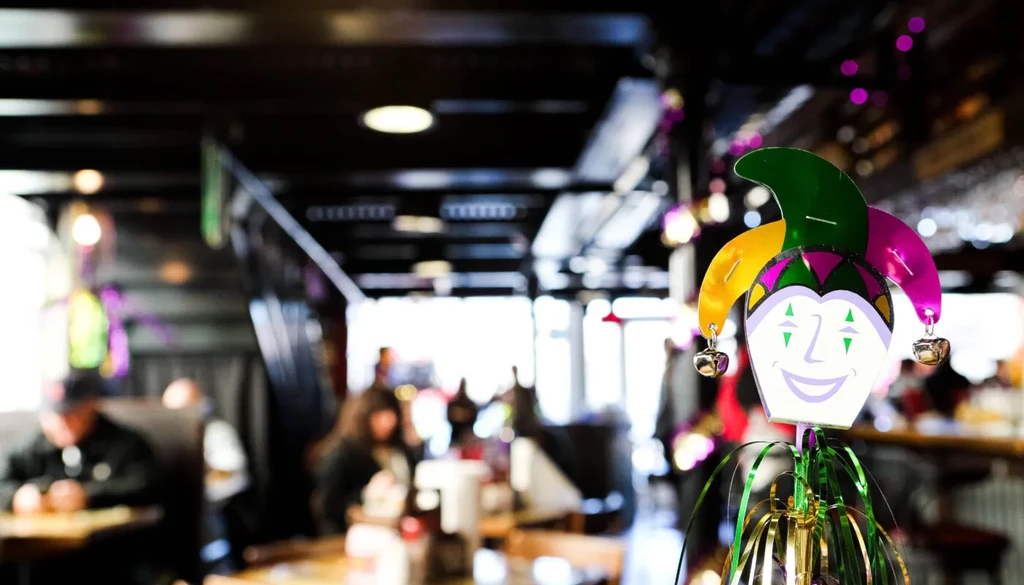 Mardi Gras jester with green and gold streamers in a blurry bar.