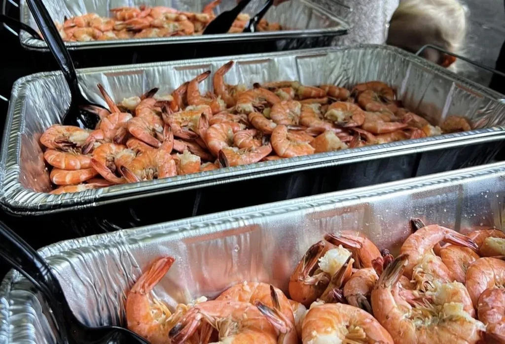 Three catering trays of plump, pinkish-orange cooked shrimp.